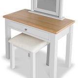 A wooden dressing table with a mirror and a matching stool, set against a white background. The table has a natural wood top, a white frame, and a single drawer.