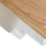 A wooden tabletop with visible grain and a small knot intersecting with a textural, beige fabric surface, set against a clean white, indistinct background.