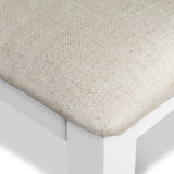 A close-up view of a textured beige cushion resting on a white, angular surface, likely furniture, with a minimalist design aesthetic.