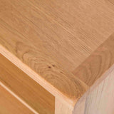 A close-up of a wooden table corner with visible wood grain texture, focusing on the detail where the tabletop meets the edge.