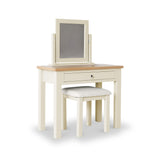 A vanity table with an upright mirror and a cushioned stool, in a two-tone cream and natural wood color, stands against a white background.