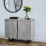 A wooden cabinet stands against a wall, atop which rests a book labeled "CHANEL," a vase with white flowers, and a small bowl, near a round mirror.