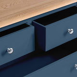 A close-up view of a navy blue drawer partially open, with round silver knobs, against a wooden tabletop.