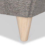 A wooden furniture leg extends from a patterned fabric, possibly a sofa or chair, against a white background.