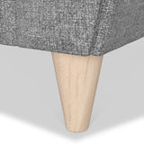 A wooden furniture leg protrudes from a gray textured fabric, showcasing a conical design and a smooth finish against a plain background.