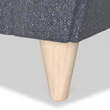 A wooden furniture leg attaches to a blue patterned fabric, likely part of a couch or chair, set against a neutral background.