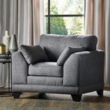 A gray upholstered armchair with plush cushions sits idle in a well-lit room featuring a side table with decorative vases and a large window draped with beige curtains.