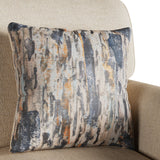 A patterned pillow rests against a beige armchair, featuring abstract blue, gray, and orange streaks. The background suggests a homey setting.