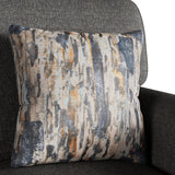 A patterned throw pillow rests against the arm of a dark grey textured sofa. The pillow features abstract streaks in blue, grey, and orange.