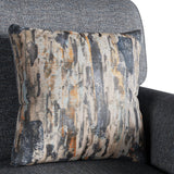 A patterned cushion resting on a grey upholstered chair, displaying abstract vertical streaks in black, white, grey, and touches of orange.