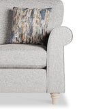 A grey upholstered armchair with a patterned cushion on a white background. The chair's design includes a rolled armrest and wooden feet.