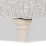 A beige, wooden furniture leg supports a section of a couch with gray upholstery against a white background.