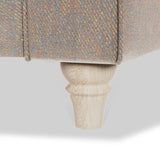 A textured, multicolored sofa fabric over a wooden conical leg against a white background.