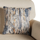 A patterned throw pillow rests on a beige armchair, evoking an abstract, bark-like design in blues, whites, and oranges.