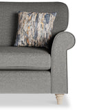 A patterned pillow rests on a gray fabric sofa with a rolled arm and wooden legs, against a white background.