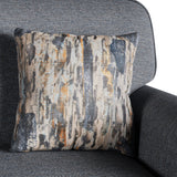 A patterned pillow rests against the back of a textured grey armchair, providing a contrast with its abstract design in beige, black, and orange hues.