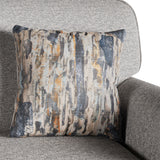 A decorative pillow with abstract pattern rests against a gray fabric chair, suggesting an indoor, home setting.