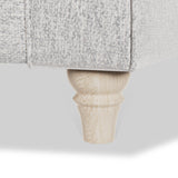 A couch leg made of natural wood supports a section of a gray woven couch against a white background.