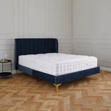 A navy blue upholstered bed with a white mattress is centered in a room with a herringbone wood floor and paneled walls. No text is present.