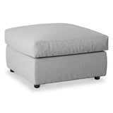 A light gray upholstered ottoman sits idly against a pure white background, featuring a tufted cushion top and short dark legs.