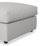 A grey upholstered ottoman with a cushioned top on short black legs, isolated against a white background.