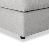 A grey fabric ottoman with a visible cushion seam, resting on a black round leg; isolated on a white background.