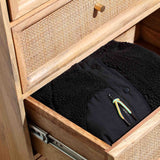 A pair of folded black fleece pants with a colorful drawstring is partly inside an open wooden drawer with a woven facade.