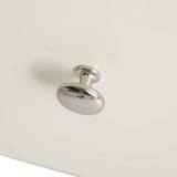 A silver drawer knob affixed to a cream-colored surface, reflecting light, no discernible action, isolated against a monochrome background.