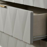 White, accordion-style radiator cover mounted against a wall next to beige fabric, with geometric shadows cast on a bright surface.