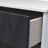 A black, rectangular object with a glossy finish is partially tucked under a white tabletop, adjacent to a textured light gray panel.