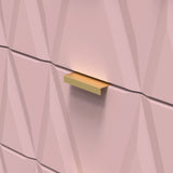 A golden shelf is mounted on a textured pink wall with geometric patterns, casting a soft shadow.